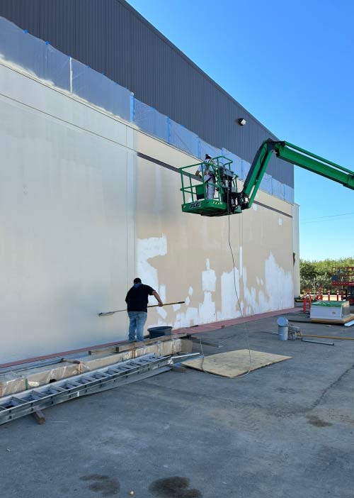 Professional painters carefully preparing the exterior surface of a business before applying a new coat of durable paint.