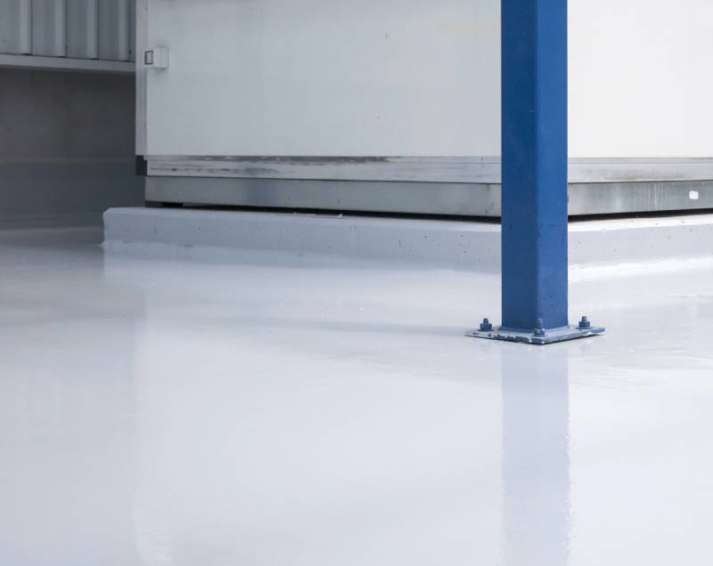 High-gloss white commercial concrete coating applied to an industrial floor with a blue structural steel post, showcasing a seamless, durable, and reflective finish.
