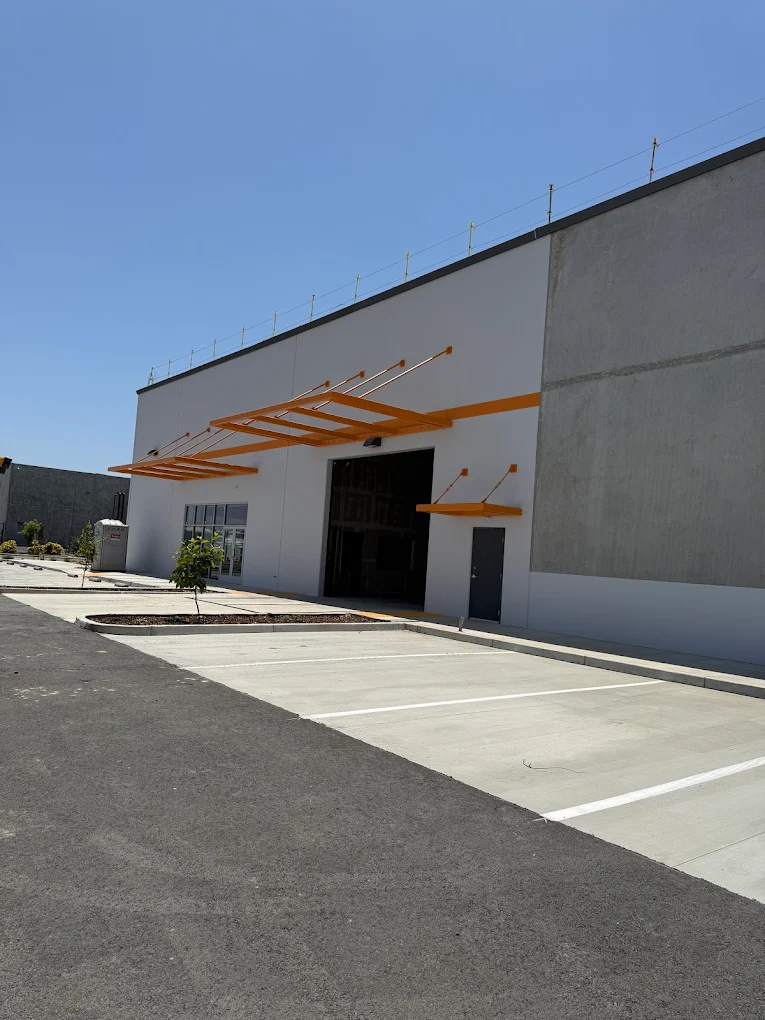 Modern commercial storefront and loading bay featuring professional white exterior painting and orange metal awnings under a clear blue sky.