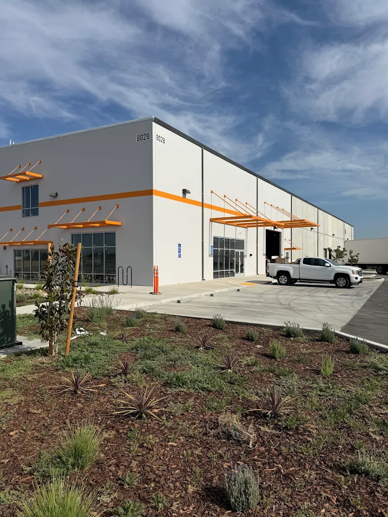 Large industrial warehouse in Sanger with a fresh white exterior and vibrant orange architectural accents painted by Ponce’s Quality Painting.